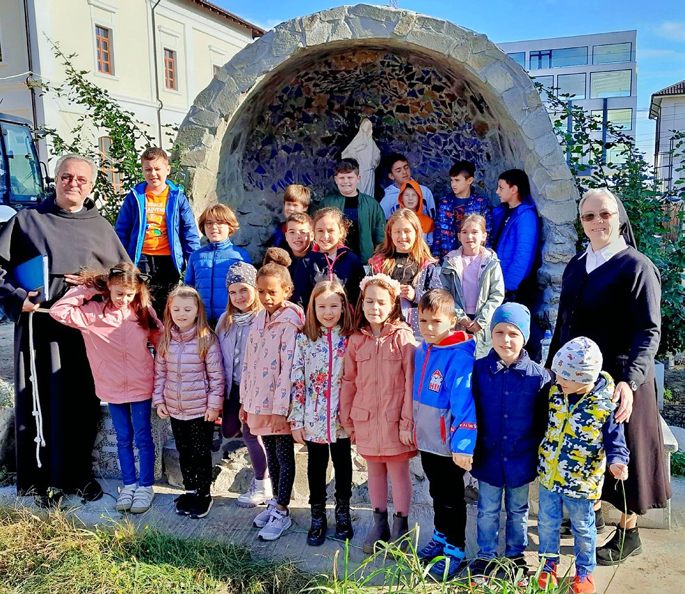 copiii după ora de religie, alături de părintele paroh Cristian Dumea și de sora Veronica, la grota Maicii Domnului de lângă biserică (noiembrie 2023)